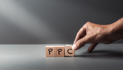 hand posing wooden blocks with acronym ppc ,pay per click ,on grey background ,e-commerce ,social media .