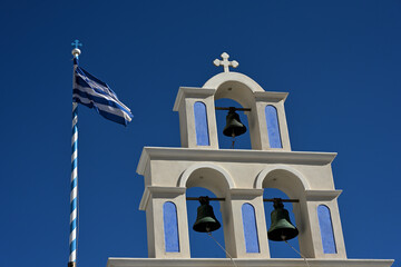 Ein typischer Glockenturm auf einer Griechischen Insel und die wehende Fahne Griechenlands im blauen Himmel.