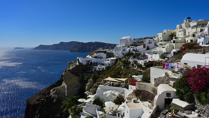 Ein wunderschönes Panorama der die Stadt Oia an der der Caldera von Santorin mit blick auf die Insel Thirasia. Man sieht auf die typischen weißen Häuser, blühende Pflanzen, bunte Wäsche auf der Leine.