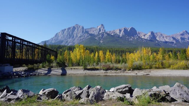 Canadian Rockies autumn landscape. Mount Rundle mountain range and trees reflected on the Bow River. Canmore, Alberta, Canada. Canmore Engine Bridge.