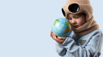 A child wearing a goggle hat holds and examines a globe. Copy space.