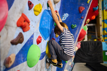 A 6-year-old boy climbing on a vibrant indoor bouldering wall with multicolored holds, engaging in a fun and active climbing experience. Perfect for kids fitness and adventure © sandsun