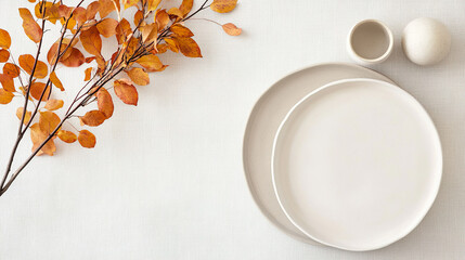 Minimalist autumn table setting with white ceramic plates and orange leaves