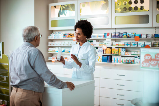 Female pharmacist showing medication bottle to senior male customer at pharmacy drugstore