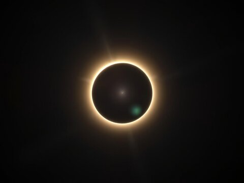 A dark disk slowly covers the sun's bright surface as totality begins, revealing an ethereal glow of light around it, cosmic event, rare occurrence