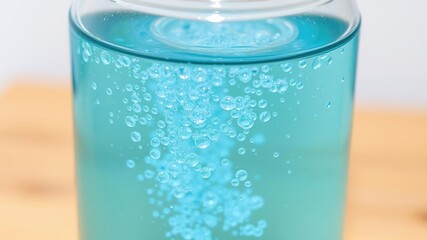Freshly filled glass jar of sparkling crystal clear blue water with numerous tiny water bubbles rising to the surface, transparent scene, calming liquid