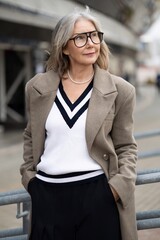 Elderly businesswoman in stylish attire stands confidently at a modern outdoor location during daylight hours