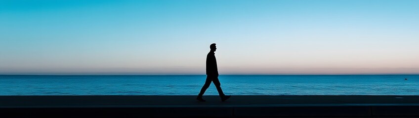 Fototapeta premium A man walks along the seafront at dusk, his silhouette against a blue sky and blue water, in a minimalist style with a panoramic view captured by a wide-angle lens. 