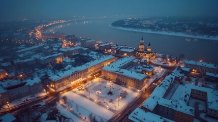 Fototapeta premium Aerial view of a snowy city at night, with a river winding through the cityscape and a church in the background.