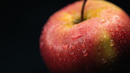A fresh red apple covered with water droplets, isolated on a black background to emphasize juiciness.