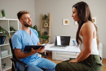 Doctor holding a clipboard and discussing diagnosis with patient during medical consultation in...