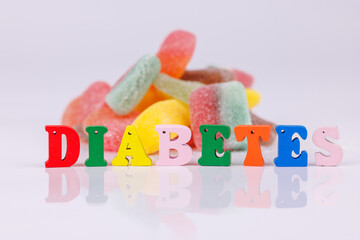 Wooden letters spelling "diabetes" with a mountain of colorful gummies in the background, set on a white surface, emphasizing sugar and health