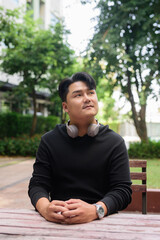 Portrait of Handsome Young Asian Man Sitting Outdoors in Park