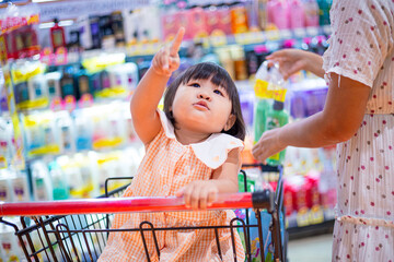 Cute girl sitting on a shopping cart in a shopping mall,Happy little child asian toddler girl, sitting in the trolley with family shopping in hypermarket.supermarket grocery store.Asian baby 