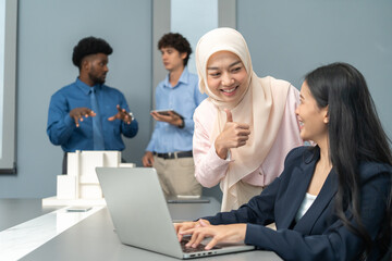 Diverse team working together, with one member giving a thumbs-up to a colleague at a laptop,...