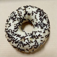 a donut with white icing and covered in chocolate sprinkles. The donut is placed on a light-colored surface