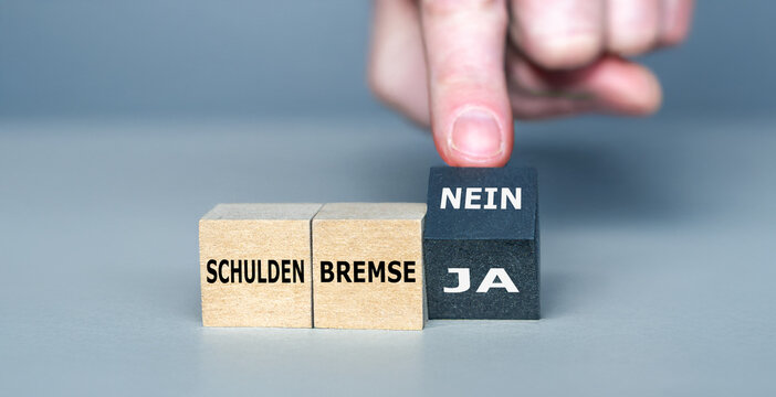 Hand dreht W&uuml;rfel und &auml;ndert den Ausdruck 'Schuldenbremse ja' in 'Schuldenbremse nein'. 