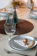 Table set for Christmas meal with plates, glasses, holiday decorations, lit candles and wine. Selective focus.