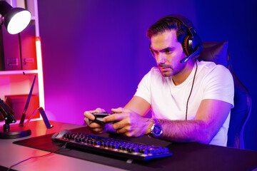 Smart gaming streamer talking with team member players with joystick to control game, mic for communicate with others on streaming live on social media at digital neon lighting studio room. Surmise.