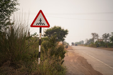 roadside pedestrian sign, rural safety road sign, pedestrian crossing ahead, countryside traffic sign, safety warning near road, triangular pedestrian symbol, highway pedestrian alert stock photo.

