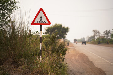 roadside pedestrian sign, rural safety road sign, pedestrian crossing ahead, countryside traffic sign, safety warning near road, triangular pedestrian symbol, highway pedestrian alert stock photo.

