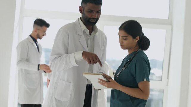Nurse woman and doctor man advise in hospital for healthcare, telehealth analysis and test results. Indian Doctors, medical team and discussion with digital tech for planning data, research and help