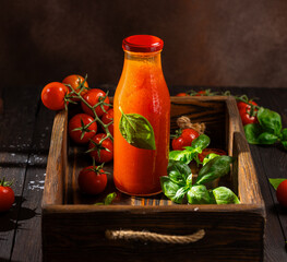 Fresh tomato juice with basil in a glass bottle on rustic wooden tray