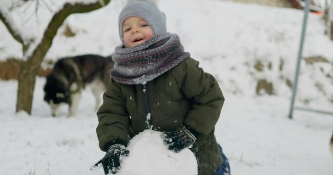 Child building snowball in winter garden