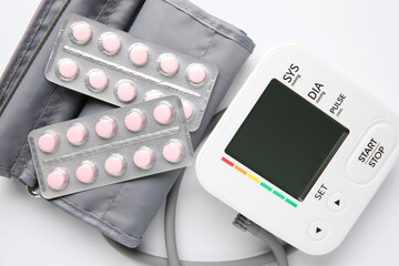 Blood pressure measuring device and pills on white background, top view
