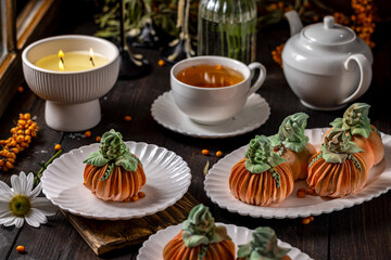 Pumpkin shaped desserts served on white plates with tea and candlelight creating cozy autumn atmosphere