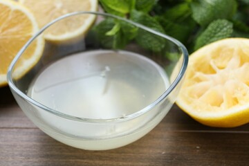 Fresh lemon juice in bowl, fruits and mint on wooden table, closeup