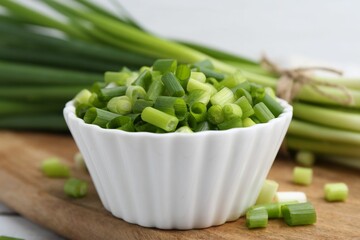 Chopped green onion in bowl and stems on table, closeup