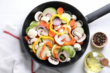 Frying pan with mix of vegetables, mushrooms and spices on white wooden table, top view