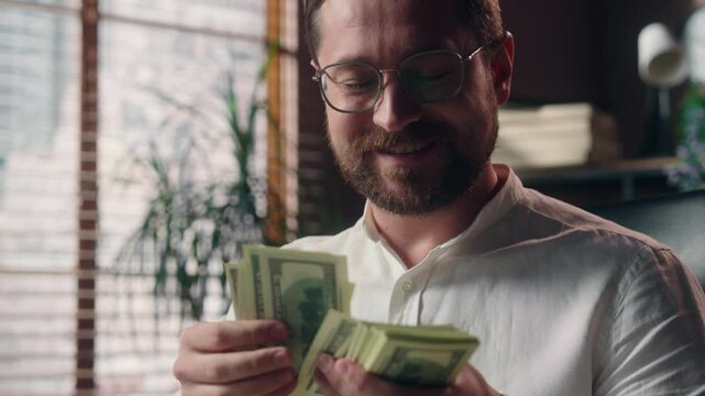 Glad Caucasian man boss accountant guy entrepreneur smiling count stack of money cash dollars payment banknotes business receiving salary male worker businessman calculating financial budget in office