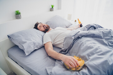 Photo of funky young man dressed nightwear lying bed sleeping after hagover indoors house apartment...