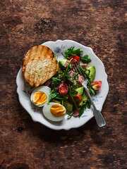 Delicious breakfast, snack - boiled egg and tuna, avocado, tomatoes, arugula salad on a wooden background, top view