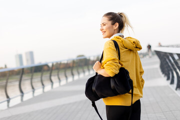 A joyful woman strolls along a modern riverside promenade at sunset, carrying a stylish bag and enjoying the serene atmosphere © BGStock72