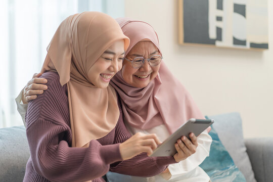 muslim mother and daughter in traditional hijab enjoy surfing internet on tablet together in the living room - Powered by Adobe
