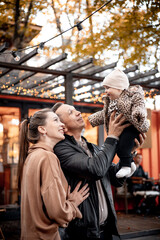 a young family with a small child in autumn in a cafe in brown and orange tones on an outdoor terrace hug and kiss, a happy family walks outside in autumn