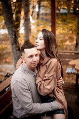 Fototapeta premium a young couple guy with a girl in autumn in a cafe in brown and orange tones on an outdoor terrace hugging and kissing, love or Valentine's day