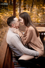 Fototapeta premium a young couple guy with a girl in autumn in a cafe in brown and orange tones on an outdoor terrace hugging and kissing, love or Valentine's day