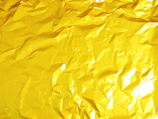Shiny crumpled yellow foil background with textured shine and vibrant color