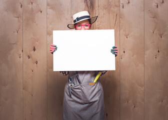 Young gardener women holding white board on wooden background in studio. Promoting female farmer...
