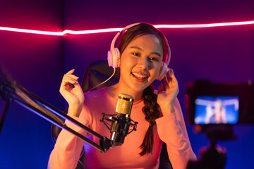 Host channel of creative broadcast listening the music on social media with listeners in positive podcast, wearing pastel color headphones, using mic radio record by camera at neon studio. Stratagem.