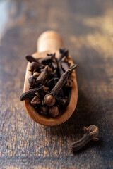 Whole cloves spice in a wooden scoop macro. Scoop full of dry clove buds close-up. Spice for herbal medicine and cooking concept. Selective focus