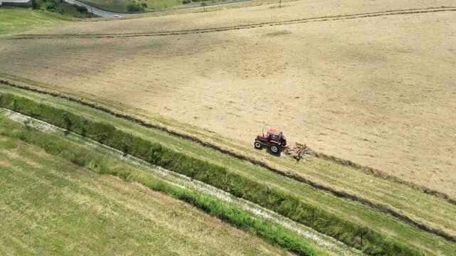 Aerial footage of a grass tedder is mowing the grass in a rural field at the daytime