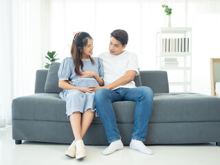 Obraz premium A happy Asian couple. Handsome husband and his beautiful wife pregnant sitting on sofa.