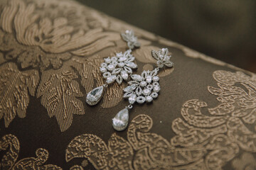 Obraz premium A pair of earrings with a flower design are displayed on a brown cloth. The earrings are made of crystal and have a drop-shaped design. The cloth is a brown color and has a floral pattern