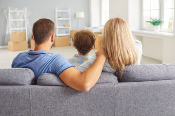 Loving close happy family sitting sofa rear view in new living room, mother, father and little son, parents with kid having rest, relax at home after moving modern flat enjoying leisure time together