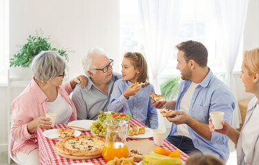Big family of different generations sitting around table with lot of food, eating and listening to...